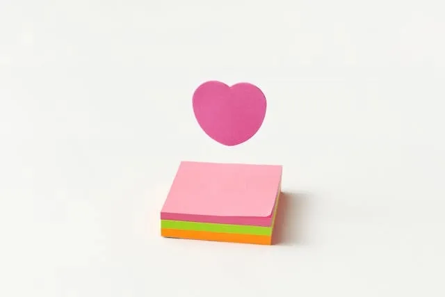 a stack of sticky notes beside a paper heart for sticky note heart