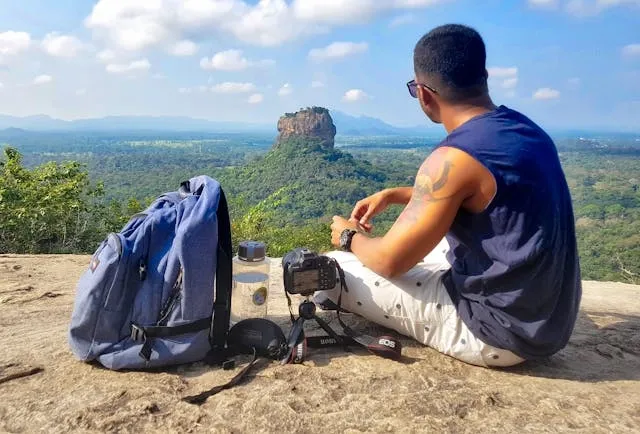 a man sitting beside a backpack atop a cliff for how to measure torso for backpack