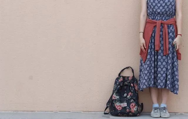 a person standing beside a backpack near a wall for how to measure torso for backpack