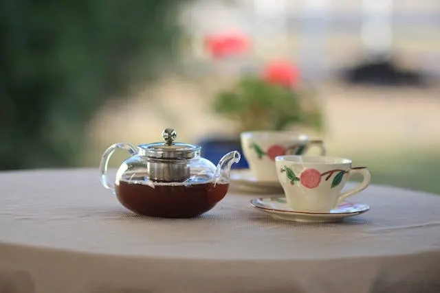 a glass teapot near teacups on a table for garden tea party