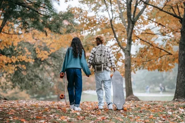 a couple carrying skateboards under trees for how to wear a backpack