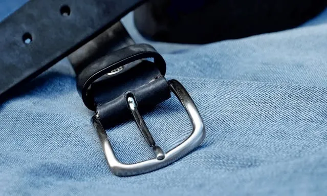a black leather belt with a silver buckle placed on top of blue denim fabric for how to put on a belt buckle