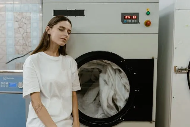 a person in a white shirt beside a washing machine for how to get gel ink out of clothes