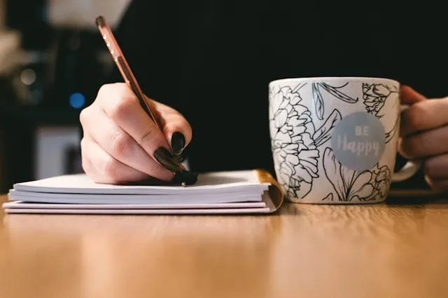 a person writing in a notepad beside a patterned mug for rollerball vs ballpoint