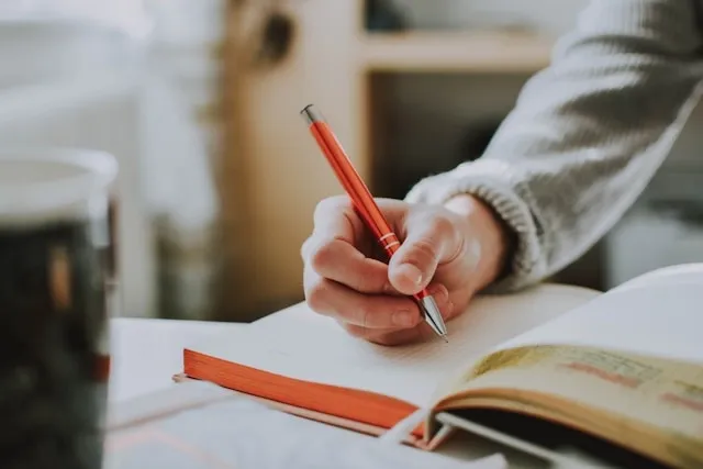 a person holding a pen to a notebook for what is a gratitude journal