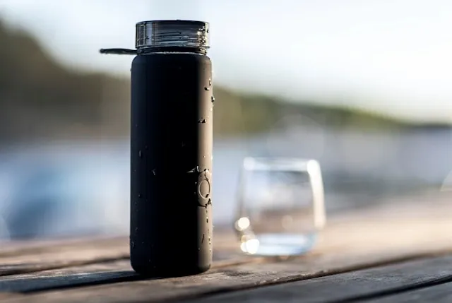a black water bottle on a wooden surface beside a glass for how to clean water bottle