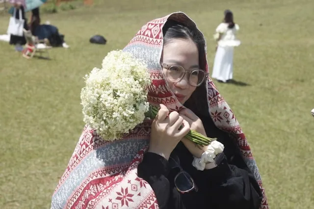 a person wrapped in a shawl while holding flowers for how to turn a scarf into a shawl