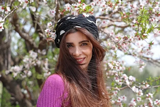 a person wearing a black and white head wrap under cherry blossoms for how to wear silk scarf on head