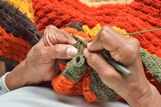 a pair of hands crocheting a blanket for how many yards of yarn for a blanket