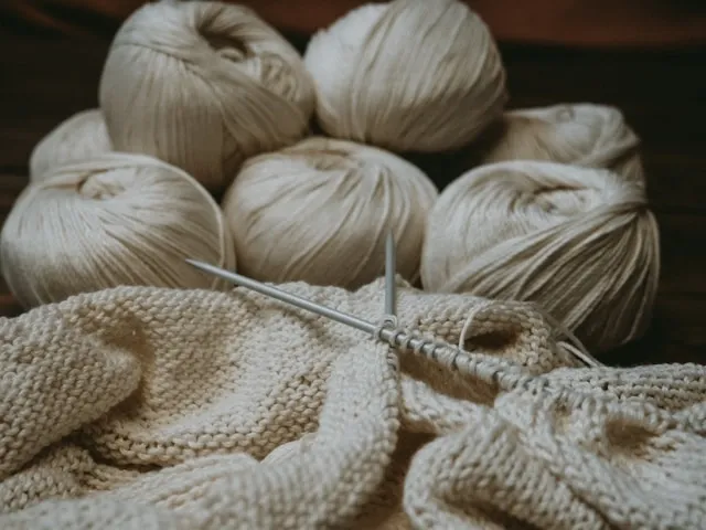 beige yarn beside some knitting work for how many yards of yarn for a blanket