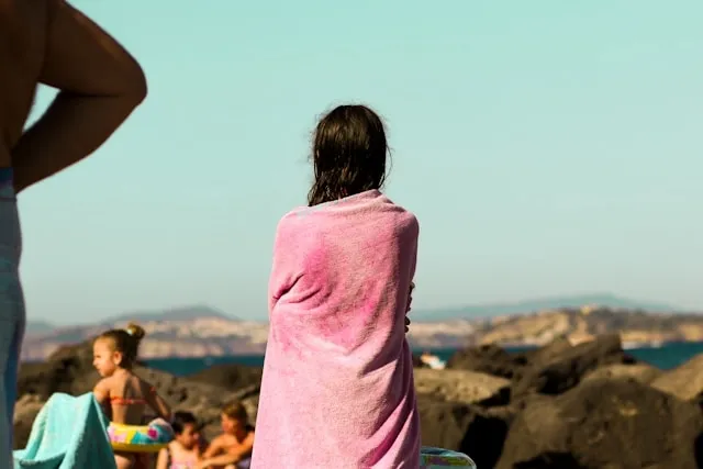 a person wrapped in a pink towel at the beach for how to soften towels