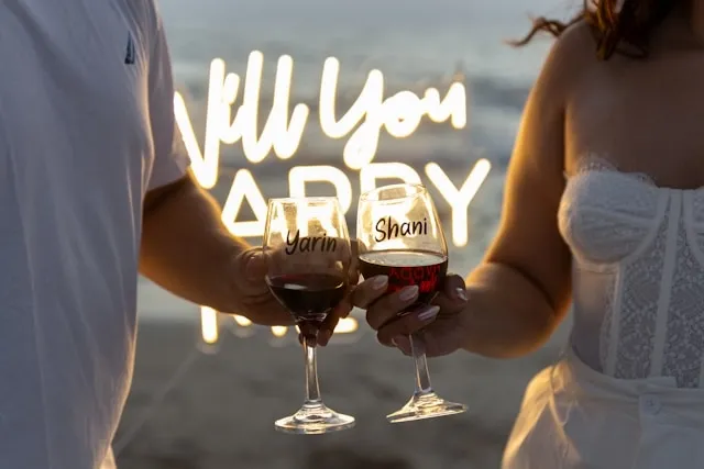 two people having a toast in front of a neon sign for valentines proposal ideas