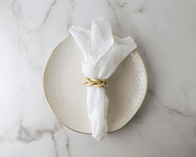 a white napkin on a beige plate for how to fold napkins with rings