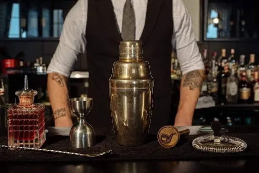 Cocktail kit gift with a metal shaker, jigger, and bitters arranged on a home bar Cocktail kit gift with a metal shaker, jigger, and bitters arranged on a home bar
