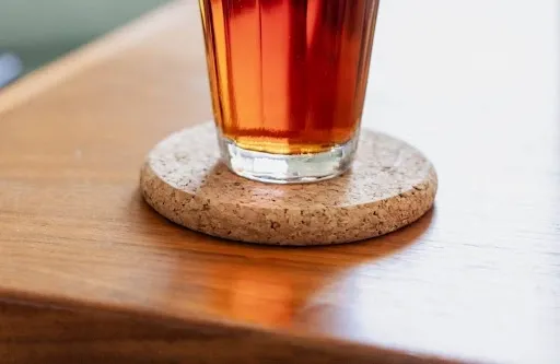 Finished cork coaster in use, with a glass of tea resting on a natural cork drink coaster on a wooden table Finished cork coaster in use, with a glass of tea resting on a natural cork drink coaster on a wooden table