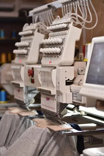 Multi-needle embroidery machine stitching a satin border on a DIY embroidered patch with colorful thread spools Multi-needle embroidery machine stitching a satin border on a DIY embroidered patch with colorful thread spools