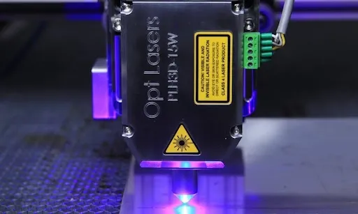 Close-up of a fiber laser engraving module with safety warning labels, the type of laser used to engrave leather patches