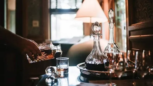 Living room whiskey lounge corner with whiskey being poured from a crystal decanter beside ambient lamp lighting, a cozy home bar cart idea
