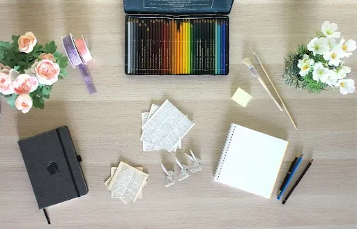 Cricut infusible ink coaster supplies laid out flat, including colored pens, brushes, transfer paper, tape and a notebook on a wooden table Cricut infusible ink coaster supplies laid out flat, including colored pens, brushes, transfer paper, tape and a notebook on a wooden table