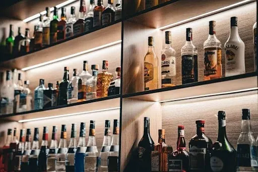 Home whiskey bar with warm-lit wood display shelves showcasing an organized bottle collection, a stylish speakeasy bar idea