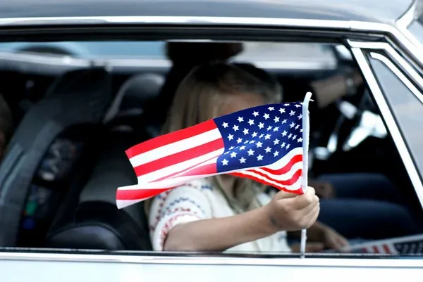 Child waving US flag out of a car window Child waving US flag out of a car window