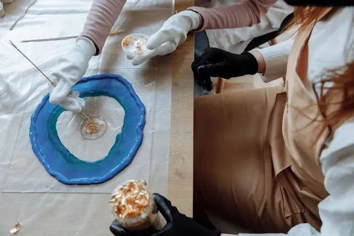 Hands adding gold leaf flakes along the edge of a blue geode resin coaster for an agate-style finish.jpg Hands adding gold leaf flakes along the edge of a blue geode resin coaster for an agate-style finish.jpg