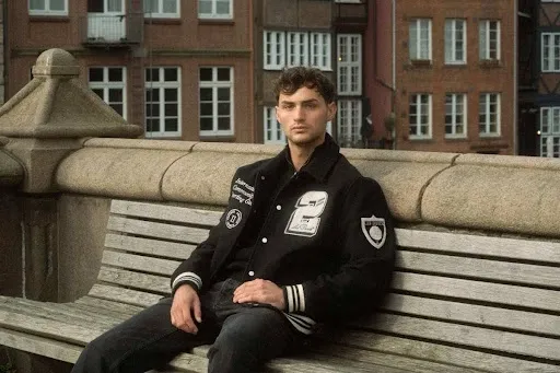 Man wearing a black wool letterman jacket decorated with plush chenille patches, showing durable heat-pressed patch placement.jpg Man wearing a black wool letterman jacket decorated with plush chenille patches, showing durable heat-pressed patch placement.jpg