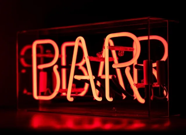A close-up of a bright red neon BAR sign glowing against a dark background
