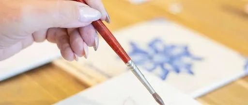 Hand painting a design onto a white ceramic tile with a fine brush, part of the decorating step for a DIY ceramic coasters project.jpg Hand painting a design onto a white ceramic tile with a fine brush, part of the decorating step for a DIY ceramic coasters project.jpg