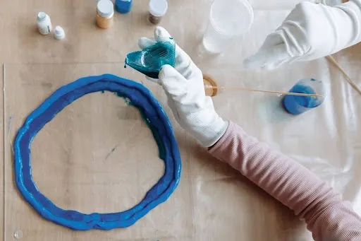 Crafter pouring layers of tinted blue epoxy resin into a silicone mold when making geode resin coasters.jpg Crafter pouring layers of tinted blue epoxy resin into a silicone mold when making geode resin coasters.jpg