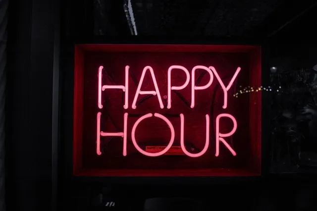 A glowing happy hour neon sign displayed above a bar counter
