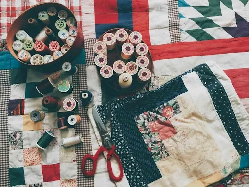 Fall quilted table runner patchwork blocks in progress with vintage thread spools, scissors, and mixed autumn-toned fabric squares on a sewing table.png