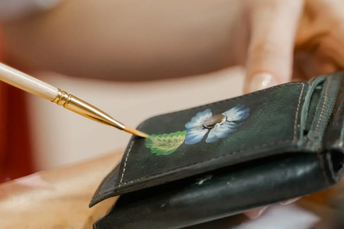 Artist hand-painting a floral design on leather with a fine brush, a technique for custom hand-painted leather coasters Artist hand-painting a floral design on leather with a fine brush, a technique for custom hand-painted leather coasters