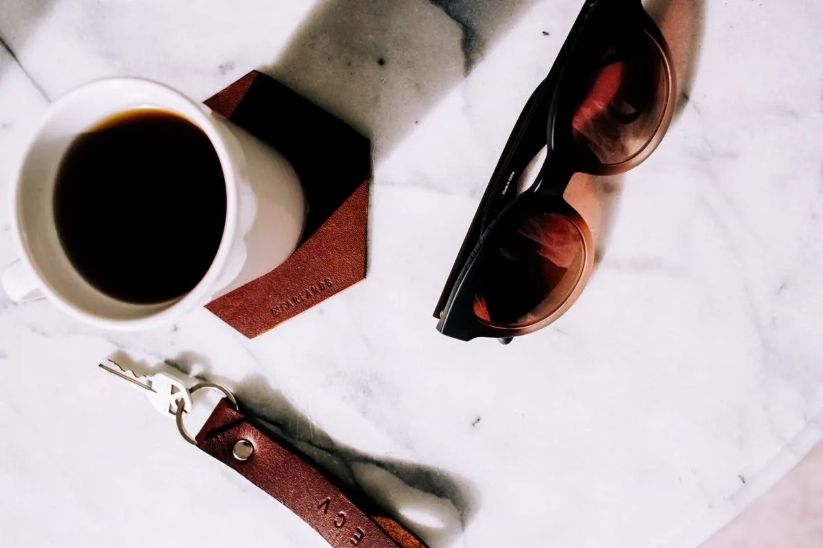 Finished leather pieces with burnished edges beside a coffee mug, showing how leather coasters age and hold up in daily use Finished leather pieces with burnished edges beside a coffee mug, showing how leather coasters age and hold up in daily use