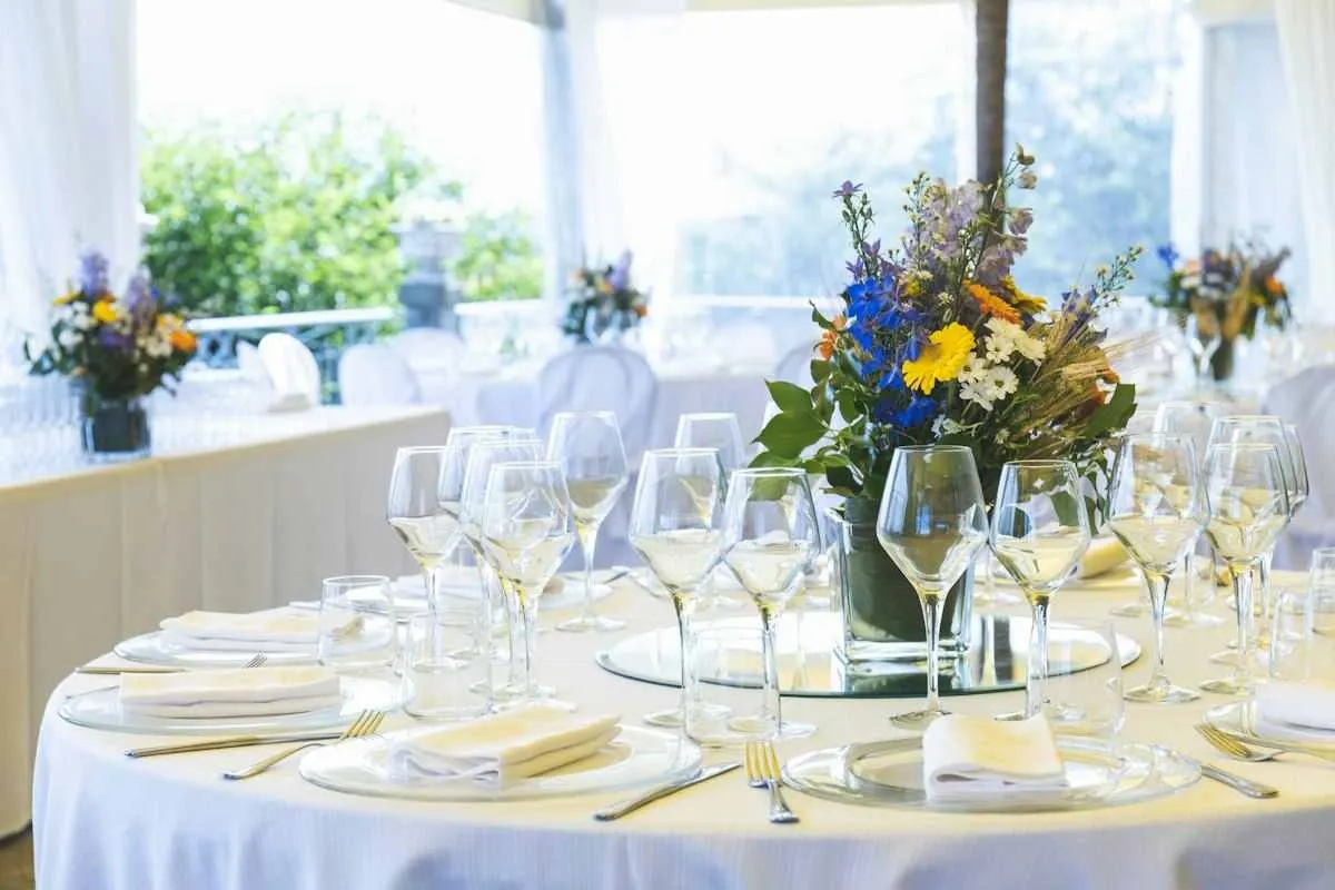 Round table with place settings and wine glasses arranged around a central floral centerpiece.jpg Round table with place settings and wine glasses arranged around a central floral centerpiece.jpg