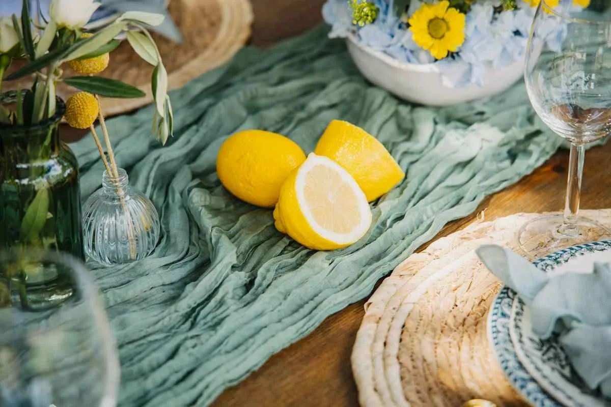 Green gauze table runner down the centre of a wooden dining table with woven placemats and lemons.jpg Green gauze table runner down the centre of a wooden dining table with woven placemats and lemons.jpg