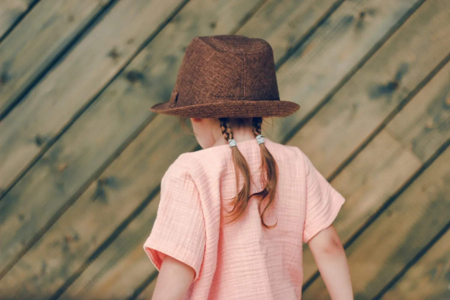 Cute little girl in rural style brown hat and muslin clothes on wooden background in a summer day