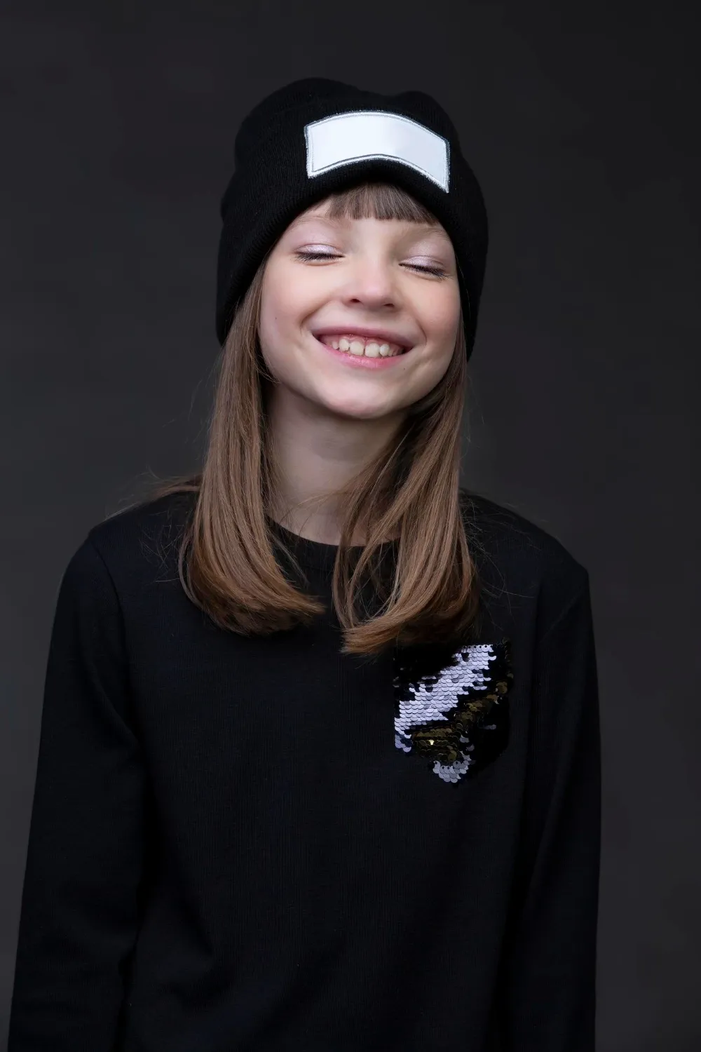 A beautiful teenager girl in a knitted hat smiles cheerfully with closed eyes
