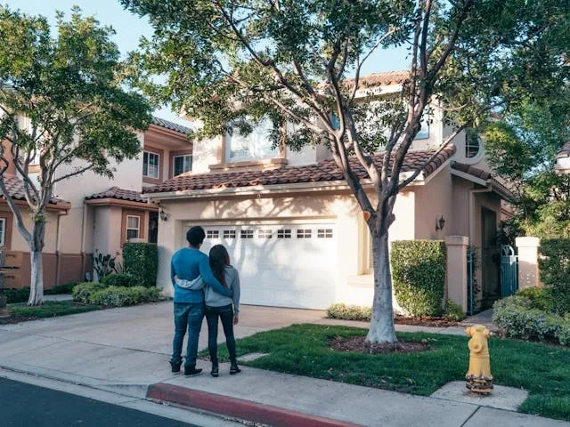 a couple standing arm in arm in front of a house for housewarming gifts for couples