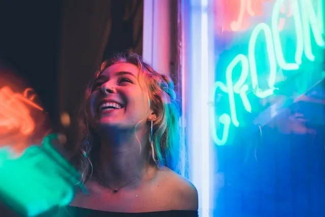 a person laughing next to a bright neon sign for how are neon signs made