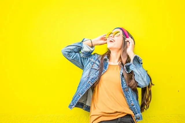 a person wearing a denim jacket in front of a bright yellow background for how to style jean jacket