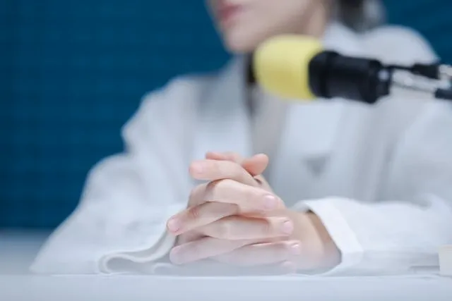 a person sitting by a microphone with their fingers interlocked for podcast room ideas