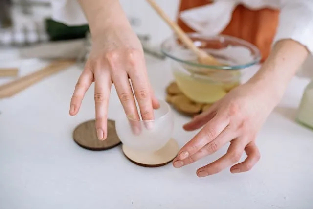 a person putting a glass container on a wood coaster atop a white table for best finish for wood coasters