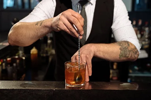 a bartender in a black waistcoat mixing a cocktail for what are the essential items needed to bartend