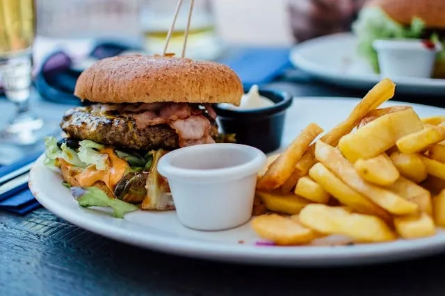 a white plate on a table with a gourmet burger and some chunky fries for fast food restaurant equipment list