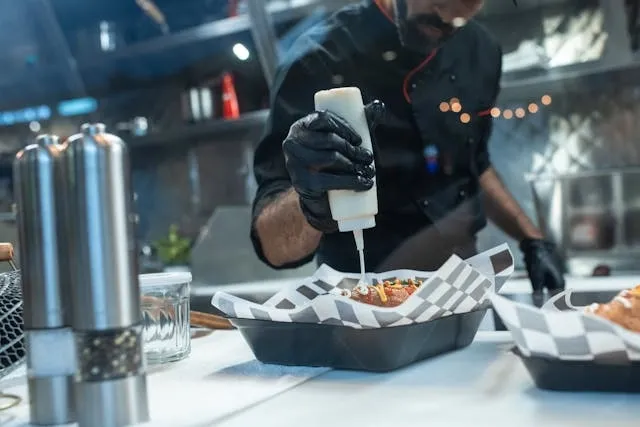 a man applying sauce to a hot dog in a commercial kitchen for fast food restaurant equipment list