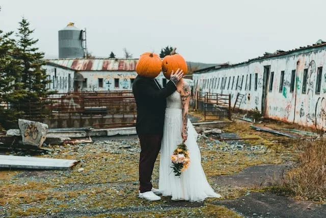 a bride and groom wearing pumpkin masks and embracing next to an abandoned train for personalized wedding ideas