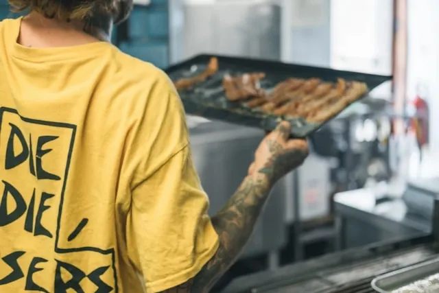 a man in a yellow t-shirt moving a tray of food in a commercial  kitche for fast food restaurant equipment list