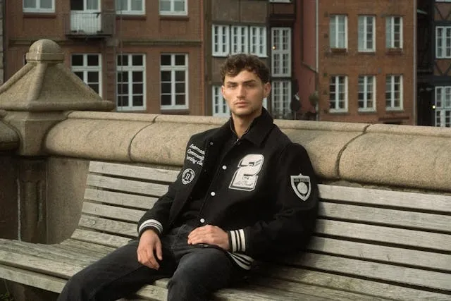 a man on a bench wearing a black jacket with white patches for how to make chenille patches