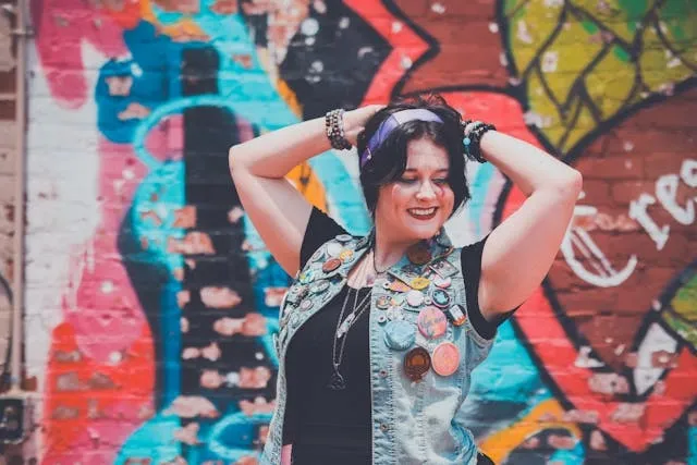 a woman wearing a denim vest with multiple patches in front of a wall with graffiti for punk patch ideas